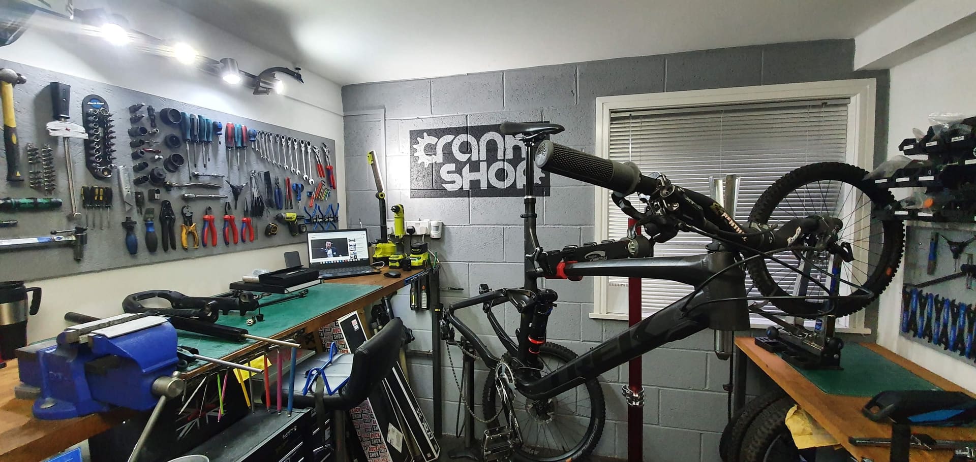 A full suspension mountain bike on the stand beneath the CrankShop sign